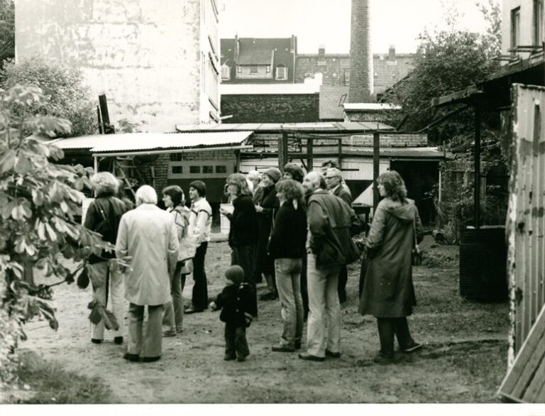Menschen stehen in einer Gruppe auf einem schwarz-weiß Foto auf einem Hinterhof in Ottensen. Das Foto zeigt einen Stadtteilrundgang des Stadtteilarchivs Ottensen aus den 80ern. Rundgänge